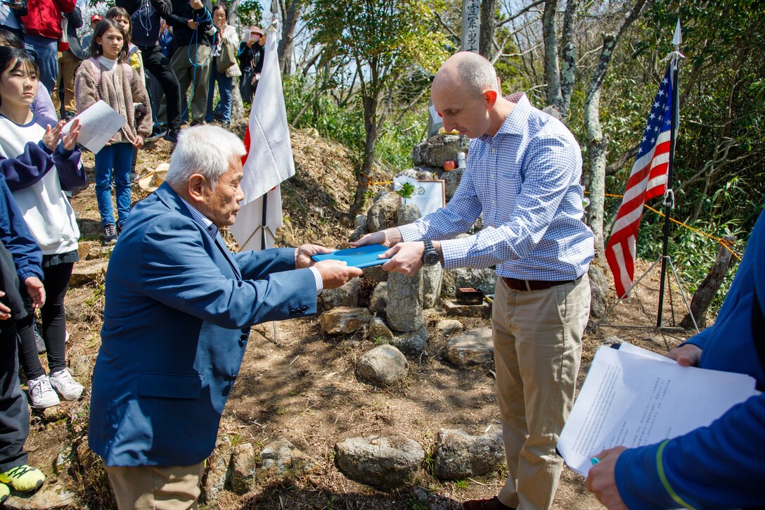 U.S. Marine Corps Maj. Matthew Forshee, right, the executive officer of Headquarters and Headquarters Squadron, Marine Corps Air Station Iwakuni and a native of Texas, hands a message from the Commander of the U.S. Naval Forces Japan to Mr. Kozo Nakagawa, the president of the Fujinowaki Neighborhood Association, during the 80th anniversary of the Marukoyama Memorial Ceremony in Kure City, Hiroshima Prefecture, Japan, April. 3, 2025. The Marukoyama Memorial Ceremony is held every year in Kure during cherry blossom season to honor the crew members of the U.S. Navy TBM-3 Avenger, Torpedo Squadron 6, who died in Kure City, Hiroshima Prefecture, Japan, on July 24, 1945. (U.S. Marine Corps photo by Sgt. Randall Whiteman)