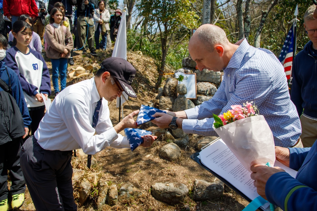 U.S. Marine Corps Maj. Matthew Forshee, right, the executive officer of Headquarters and Headquarters Squadron, Marine Corps Air Station Iwakuni and a native of Texas, receives an American flag from Fukao Hiroyuki, the U.S. participation coordinator for the Marukoyama Memorial Ceremony, during the 80th anniversary of the Marukoyama Memorial Ceremony in Kure City, Hiroshima Prefecture, Japan, April. 3, 2025. The Marukoyama Memorial Ceremony is held every year in Kure during cherry blossom season to honor the crew members of the U.S. Navy TBM-3 Avenger, Torpedo Squadron 6, who died in Kure City, Hiroshima Prefecture, Japan, on July 24, 1945. (U.S. Marine Corps photo by Sgt. Randall Whiteman)