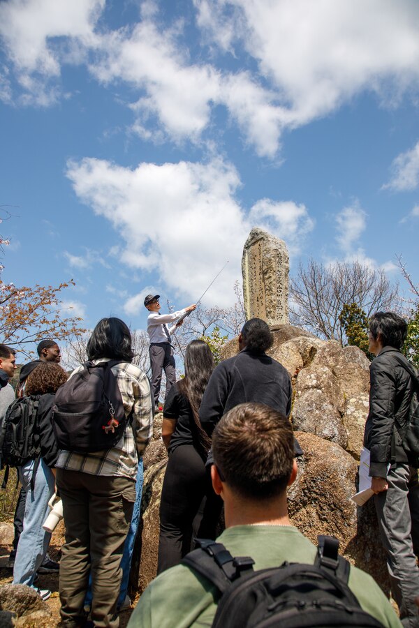 Fukao Hiroyuki, the U.S. participation coordinator for the Marukoyama Memorial Ceremony for the Marukoyama Memorial ceremony, explains the inscription on the Furukawa family memorial to the U.S. Marines and Sailors from Marine Corps Air Station Iwakuni after the 80th anniversary of the Marukoyama Memorial Ceremony in Kure City, Hiroshima Prefecture, Japan, April. 3, 2025. The Marukoyama Memorial Ceremony is held every year in Kure during cherry blossom season to honor the crew members of the U.S. Navy TBM-3 Avenger, Torpedo Squadron 6, who died in Kure City, Hiroshima Prefecture, Japan, on July 24, 1945. (U.S. Marine Corps photo by Sgt. Randall Whiteman)