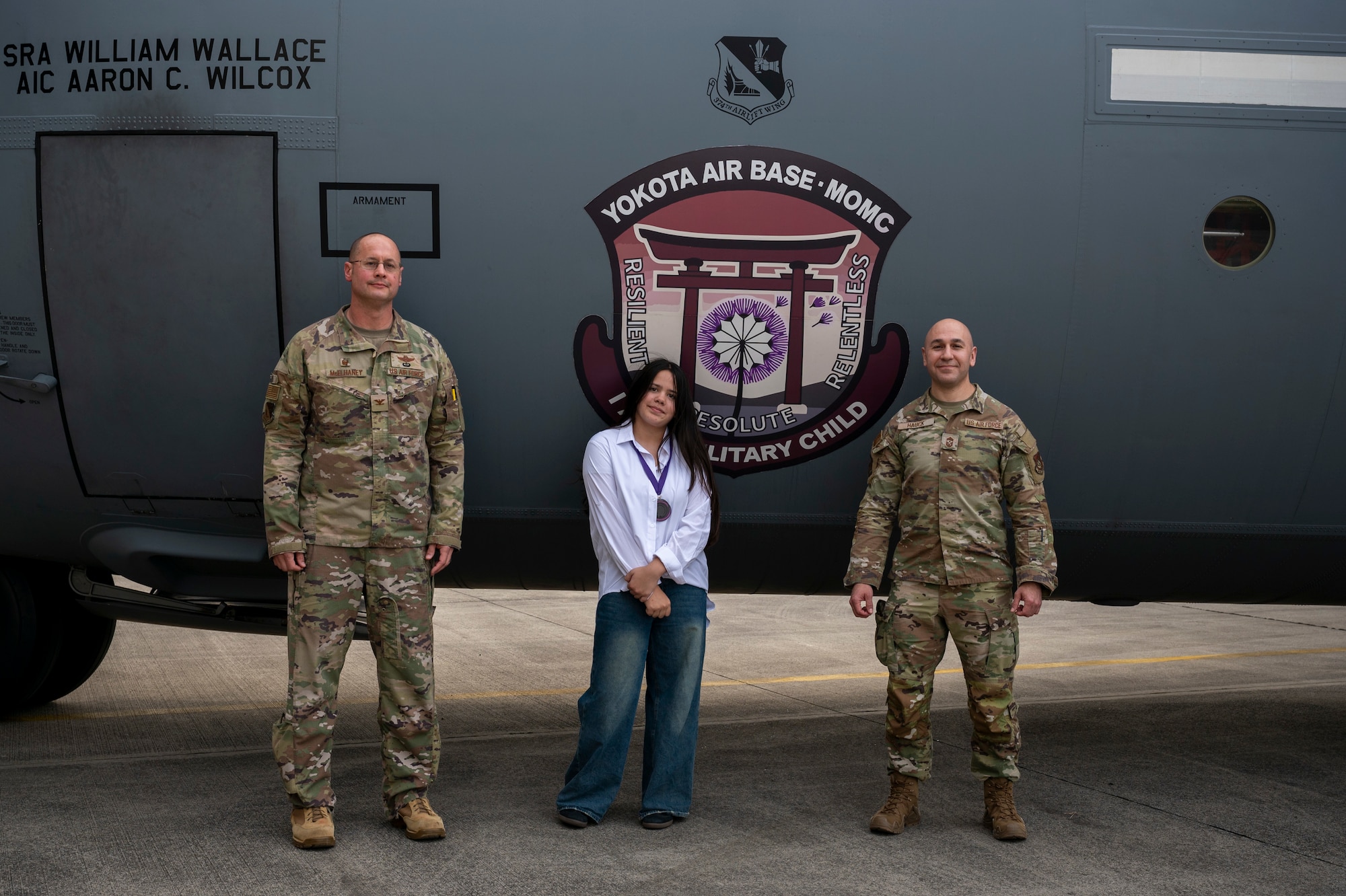 Two military members and a student pose in front of a patch decal on a C-130J aircraft.