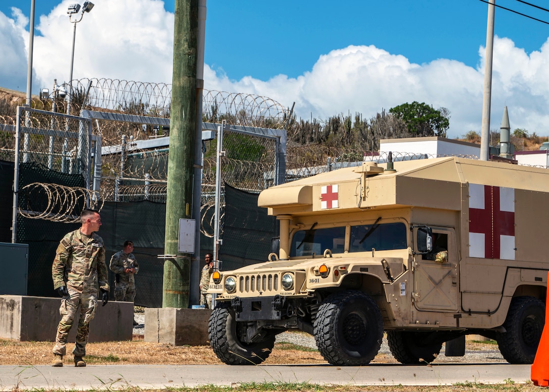 Service members stand next to a bus outside of a fenced area during daylight.