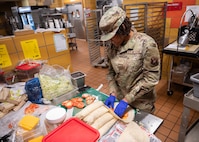 An Airman prepares turkey and cheese wraps in a dining facility kitchen.