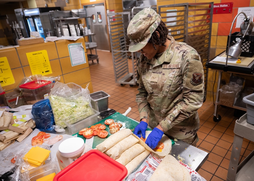 An Airman prepares turkey and cheese wraps in a dining facility kitchen.