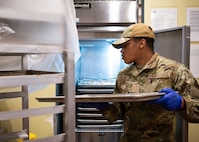 An Airman places a tray of pizza into a refrigerator as a base dining facility.