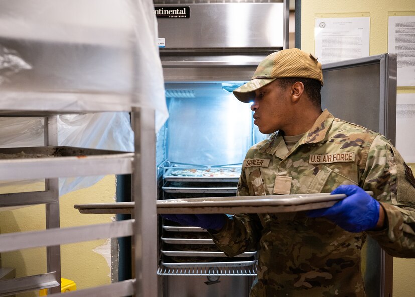 An Airman places a tray of pizza into a refrigerator as a base dining facility.