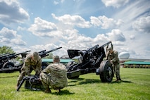 Army soldiers from the Presidential Salute Battery, dressed in combat uniforms, are adjusting the position of a black, modified 3-inch M5 anti-tank gun that is placed on a green lawn.