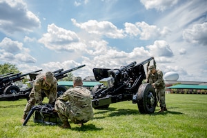 Army soldiers from the Presidential Salute Battery, dressed in combat uniforms, are adjusting the position of a black, modified 3-inch M5 anti-tank gun that is placed on a green lawn.