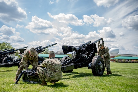 Army soldiers from the Presidential Salute Battery, dressed in combat uniforms, are adjusting the position of a black, modified 3-inch M5 anti-tank gun that is placed on a green lawn.