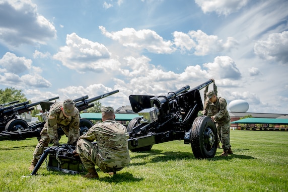 Army soldiers from the Presidential Salute Battery, dressed in combat uniforms, are adjusting the position of a black, modified 3-inch M5 anti-tank gun that is placed on a green lawn.
