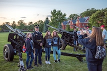 Army soldiers dressed in dark ceremonial uniforms are posing for pictures with audience members next to the Presidential Salute Battery's modified 3-inch M5 anti-tank guns after a Twilight Tattoo show.