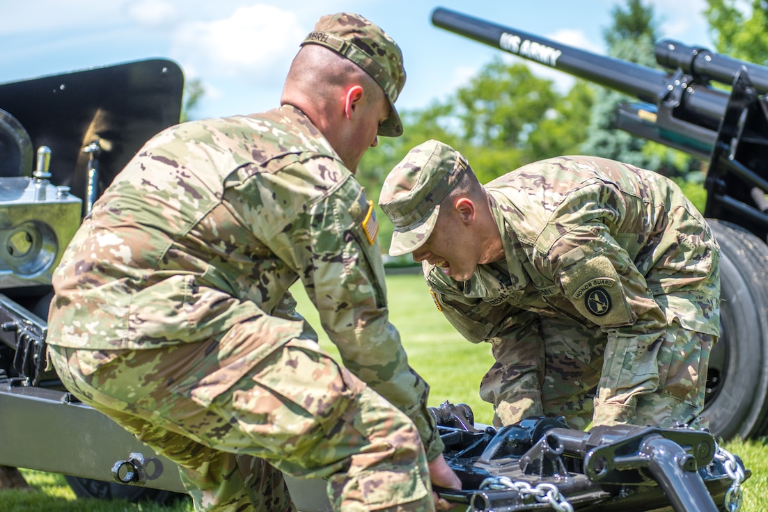 Two soldiers dressed in Army combat uniforms are lifting a modified 3-inch M5 anti-tank gun while preparing for a performance with the Presidential Salute Battery.