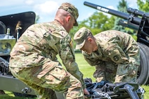 Two soldiers dressed in Army combat uniforms are lifting a modified 3-inch M5 anti-tank gun while preparing for a performance with the Presidential Salute Battery.