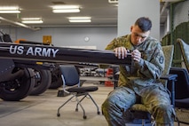 An Army Soldier is working on the barrel of a modified 3-inch M5 anti-tank gun inside a maintenance shop for the Presidential Salute Battery.