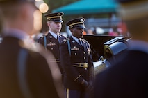 Army soldiers in dark ceremonial uniforms are standing near Army modified 3-inch M5 anti-tank guns as part of the Presidential Salute Battery.