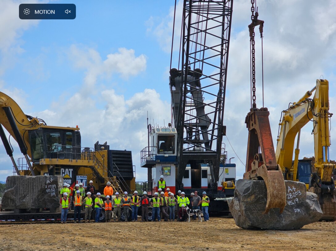 USACE engineers stand in front of an excavator with one of the boulders used on the south jetty.