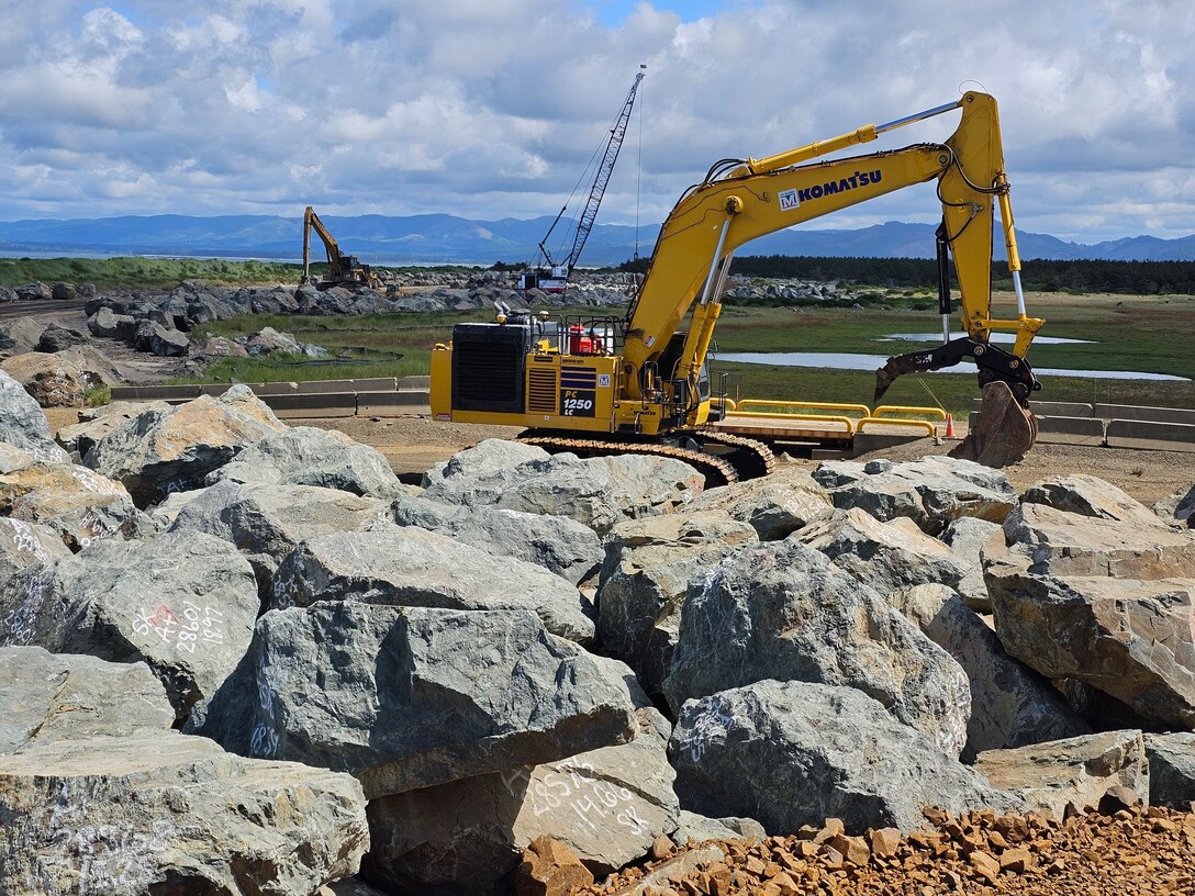 Large boulders with several pieces of heavy equipment are pictured.