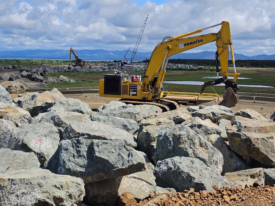 Large boulders with several pieces of heavy equipment are pictured.