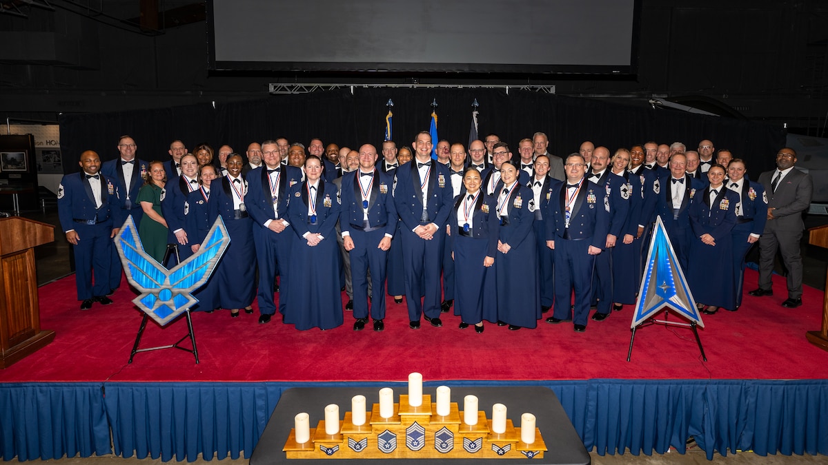 A large group photo of military members in formal wear on stage with large U.S. Air Force and Space Force insignias on either side