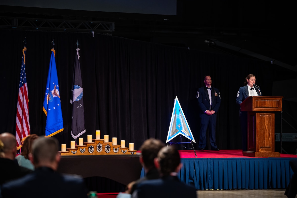 A wide-angle image of a stage with the U.S., Air Force, and Space Force flags. A tiered candle holder with military ranks, and two formally dressed military members