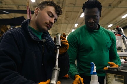 Aviation Structural Mechanic 3rd Class Shea Fortin, left, and Aviation Structural Mechanic 2nd Class Lancing Guedet, both assigned to the “Tridents” of Helicopter Sea Combat Squadron (HSC) 9, inspect a pylon lock pin on an MH-60S Sea Hawk during routine maintenance in the hangar bay of the world's largest aircraft carrier, USS Gerald R. Ford (CVN 78), March 18, 2025.