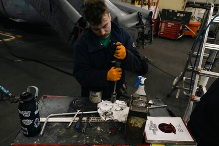 Aviation Structural Mechanic 3rd Class Shea Fortin, assigned to the “Tridents” of Helicopter Sea Combat Squadron (HSC) 9, disassembles the housing of a pylon lock pin on an MH-60S Sea Hawk during routine maintenance in the hangar bay of the world's largest aircraft carrier, USS Gerald R. Ford (CVN 78), March 18, 2025.