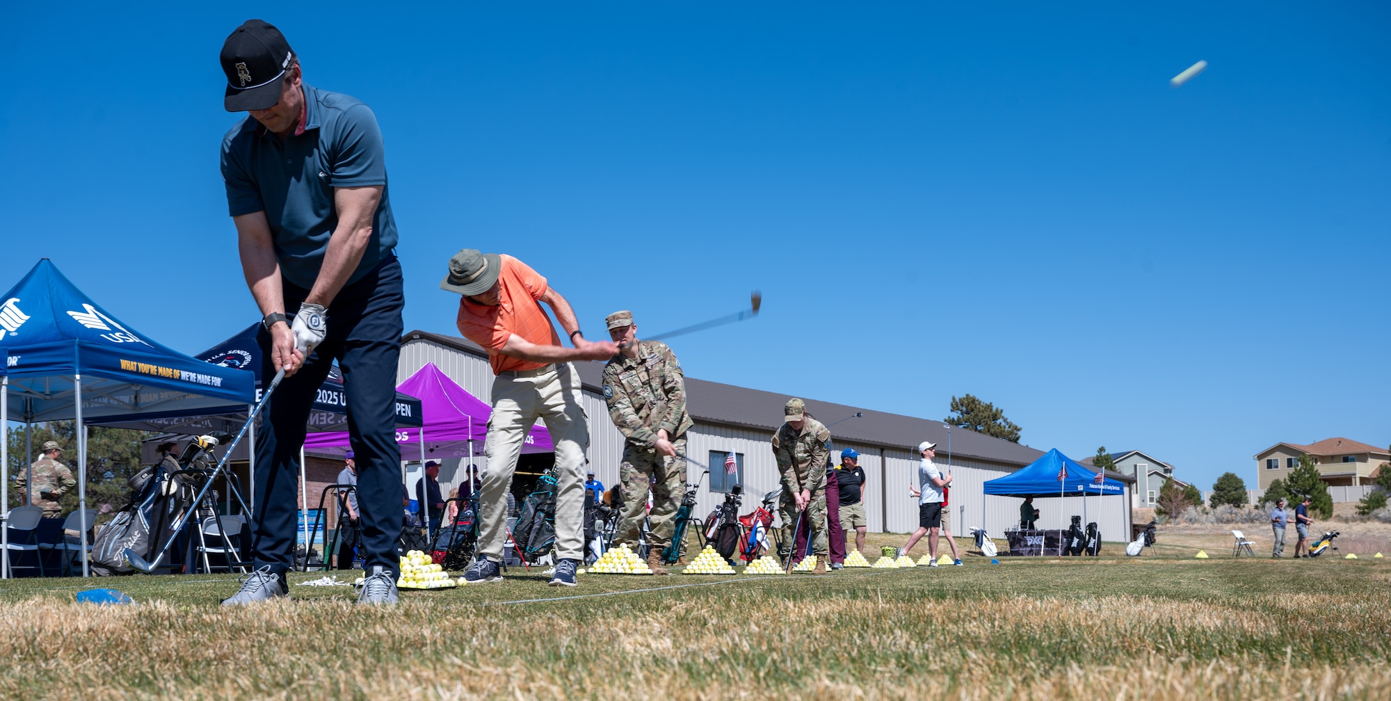 A group of people swing golf clubs and hit golf balls on the driving range.