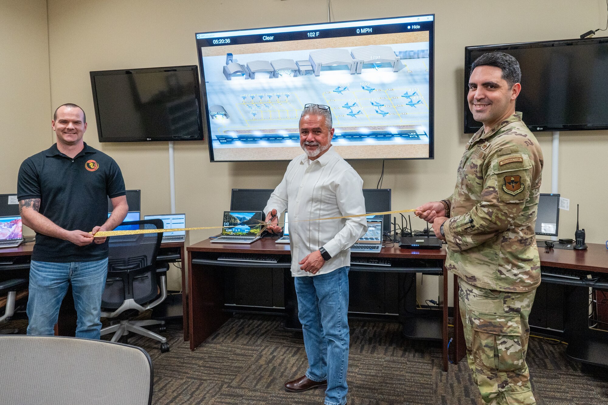 Mateo Gonzalez, 318th Training Squadron, stands ready to cut the ribbon during the official ribbon cutting to showcase new, upgraded software for the Aircraft Maintenance Officer Course simulator. Gonzalez is joined by Master Sgt. Jeremy Sampson, 423rd Training Squadron, and Tech. Sgt. Joseph Torres-Santiago. The acquisition was a result of a collaborative effort between the Inter-American Air Forces Academy and the Air Mobility Command which enabled the Expeditionary Operations School to share its resources. (U.S. Air Force photo by Vanessa R. Adame)