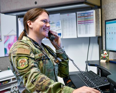 Uniformed service member answers phone standing in front of computer screen