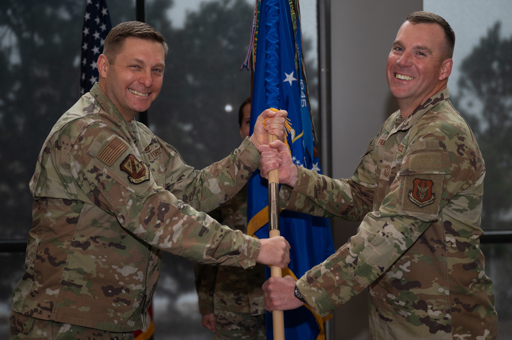 Two men in military uniforms smile while they hold a guidon.