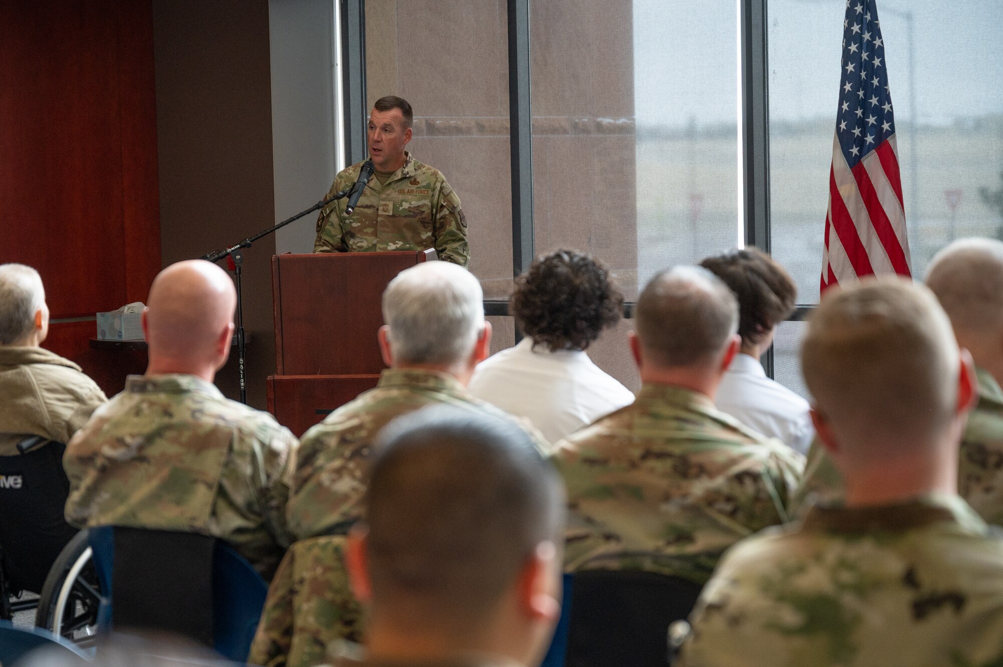 A man in a military uniform speaks at a podium in front of an audience.