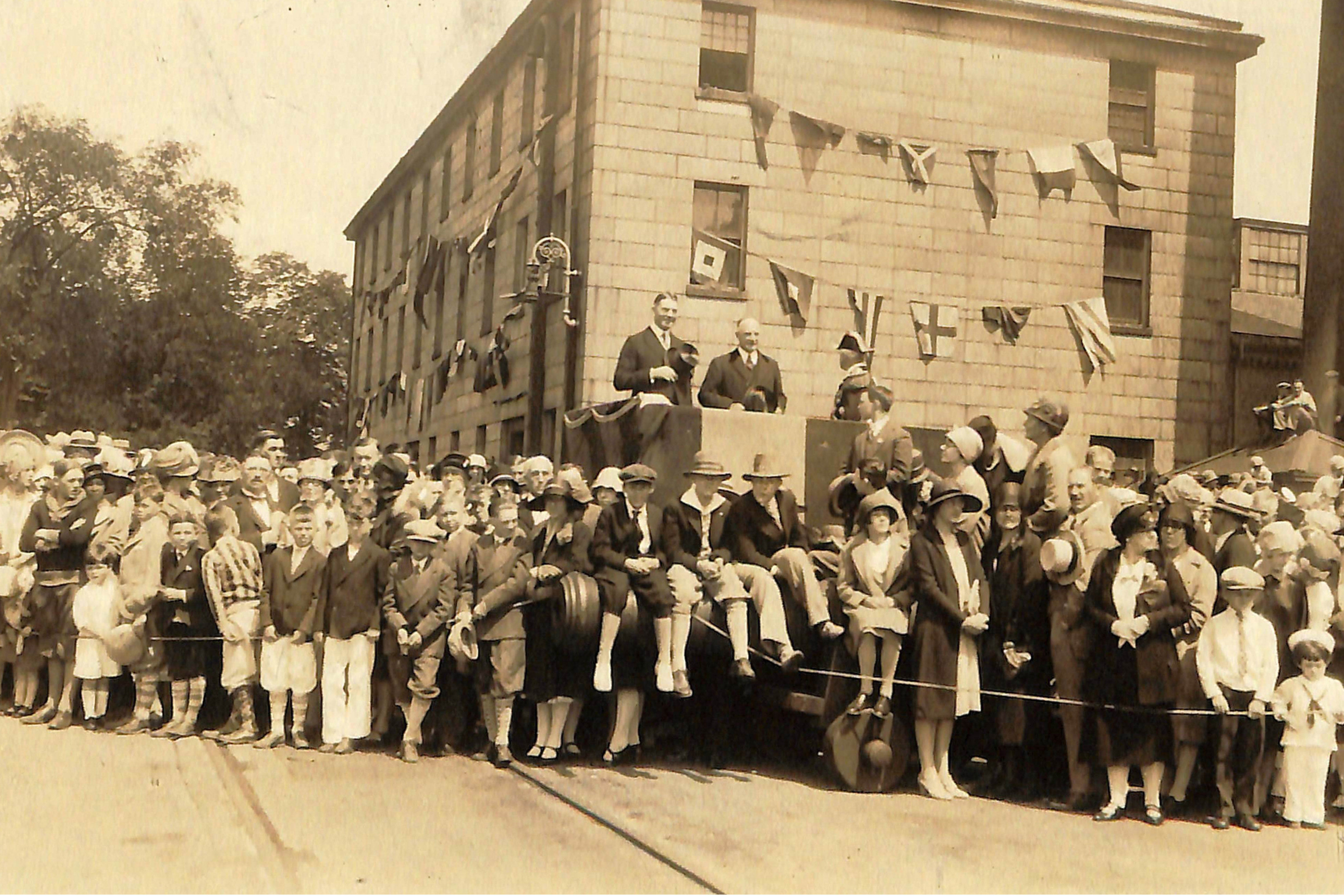 An old photo shows a group of people and children posing in a street.
