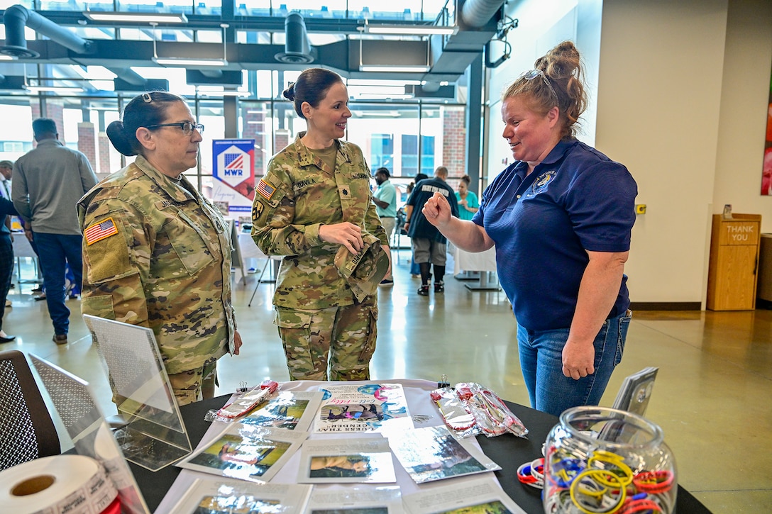 Two women in Army uniforms talk to a woman in a blue shirt and jeans