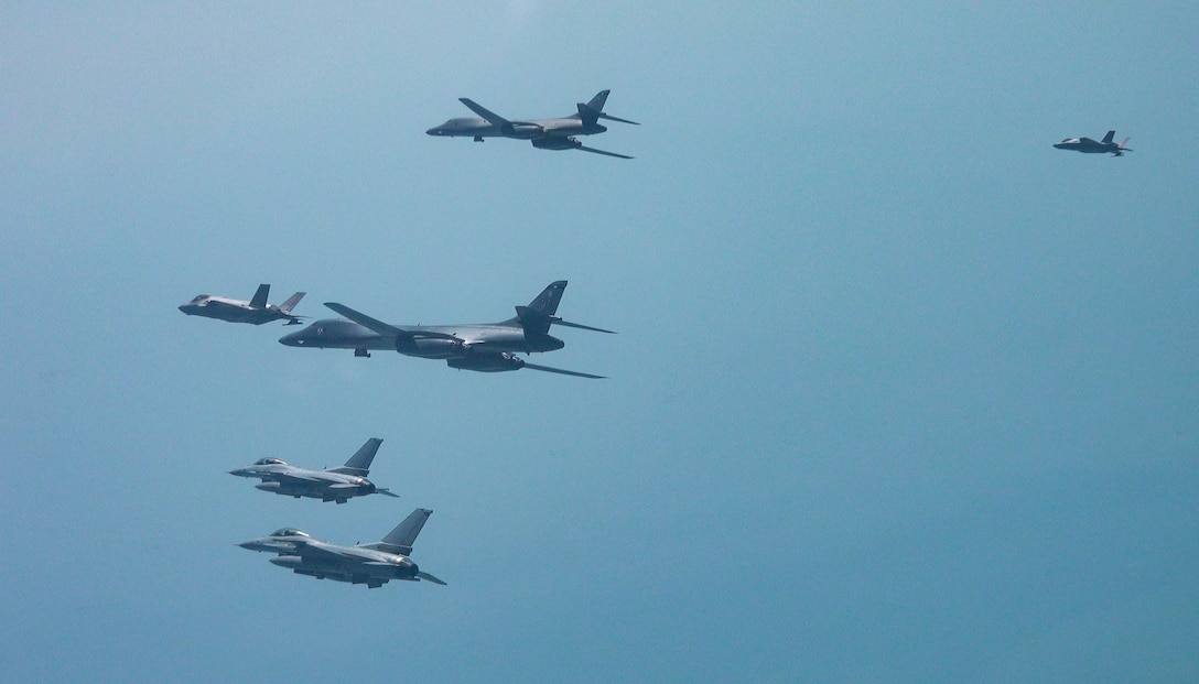 Five aircraft fly in formation from the side view in front of a blue-green hazy sky.