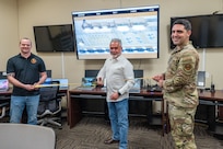 Mateo Gonzalez, 318th Training Squadron, stands ready to cut the ribbon during the official ribbon cutting to showcase new, upgraded software for the Aircraft Maintenance Officer Course simulator. Gonzalez is joined by Master Sgt. Jeremy Sampson, 423rd Training Squadron, and Tech. Sgt. Joseph Torres-Santiago. The acquisition was a result of a collaborative effort between the Inter-American Air Forces Academy and the Air Mobility Command which enabled the Expeditionary Operations School to share its resources. (U.S. Air Force photo by Vanessa R. Adame)