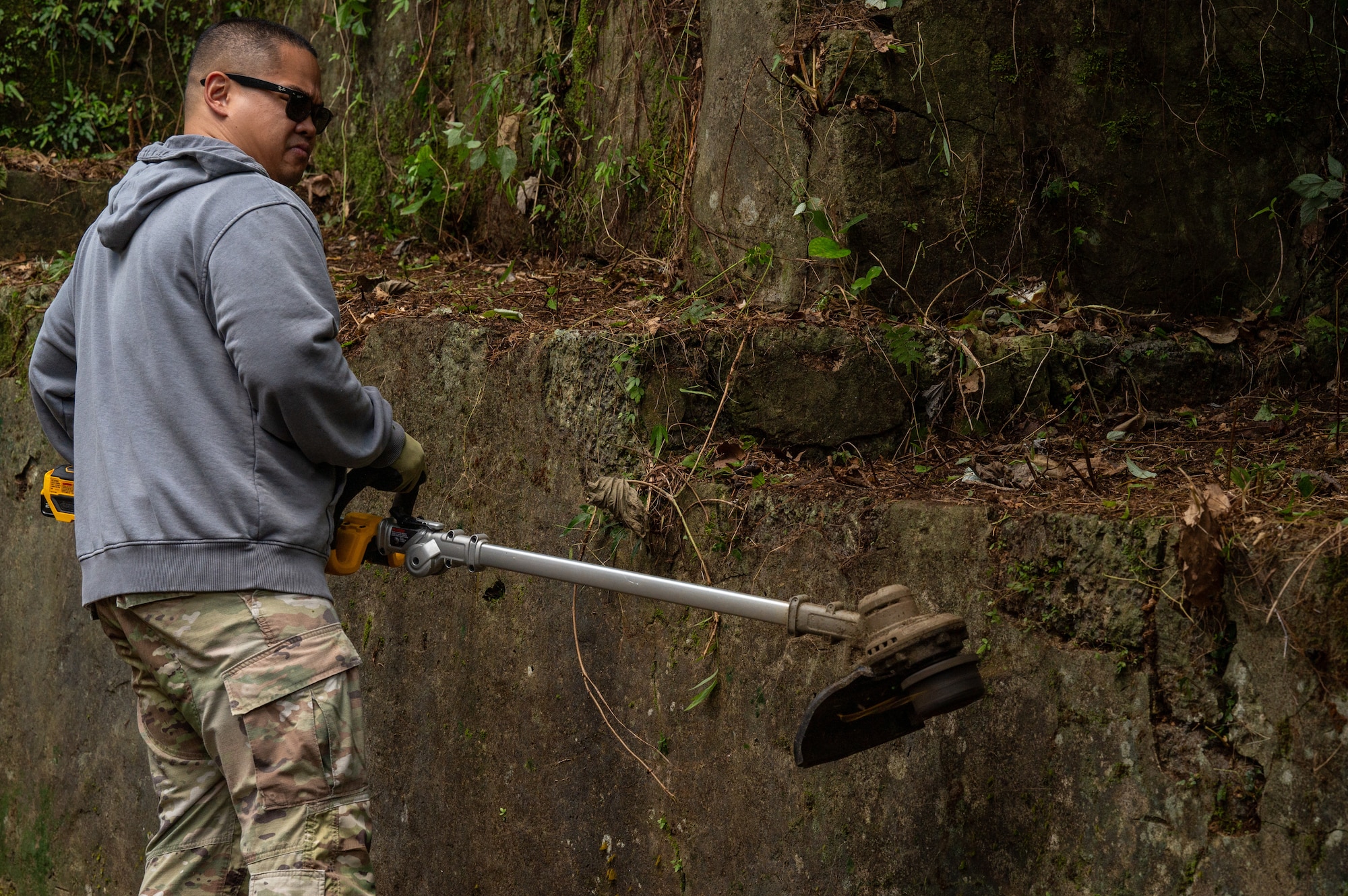 An airman using a grass cutter to clear vegetation from a tomb