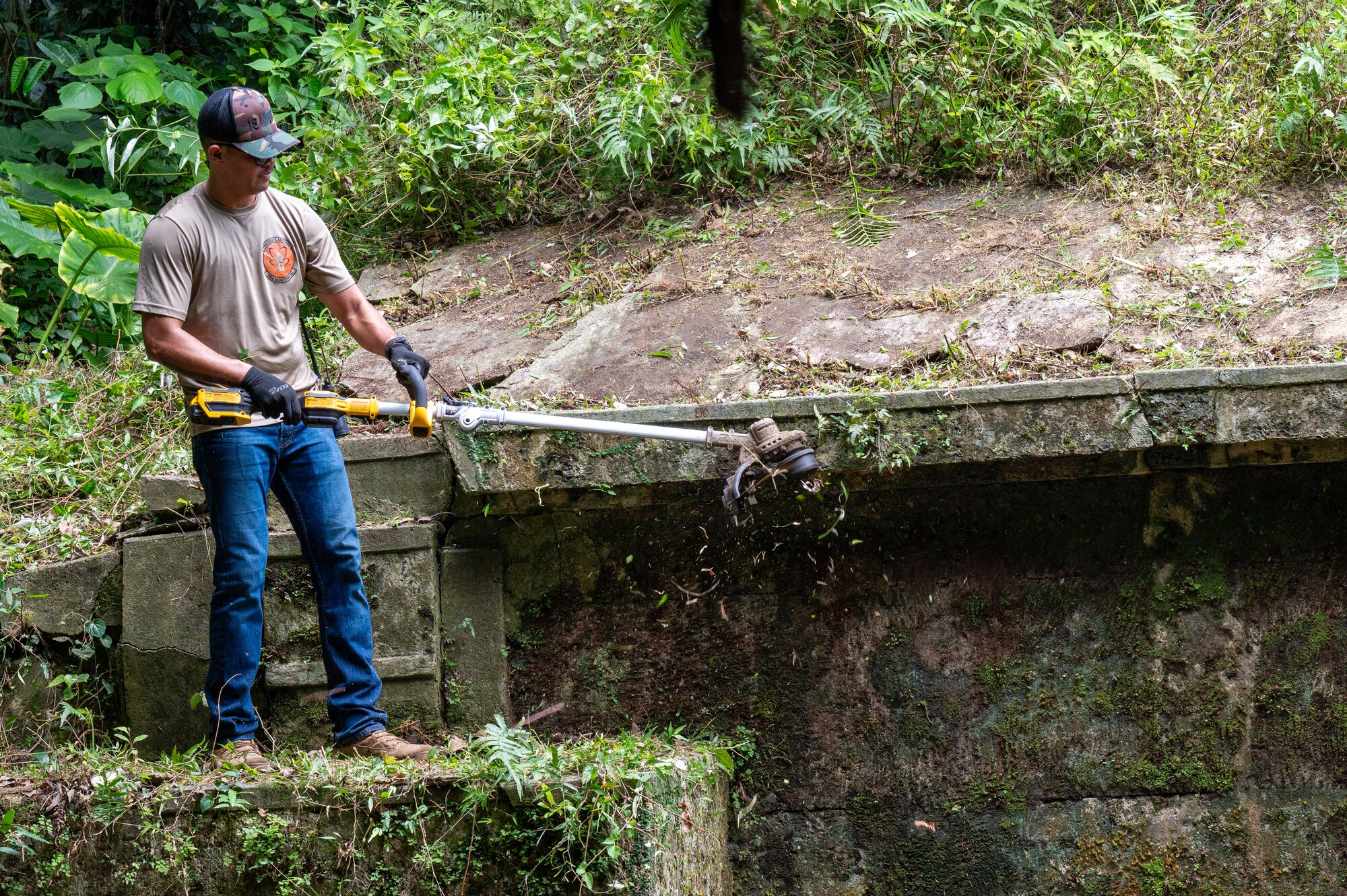 Airmen using a grass cutter to clear vegetation at a tomb