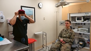 Doctor puts on mask while Airman sits in chair. (U.S. Air Force photo by Senior Airman Ian Sullens)
