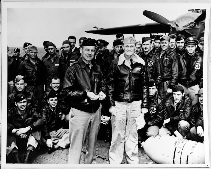 Black and white image showcasing Lieutenant Colonel James H. Doolittle (left front), leader of the attacking force, and Captain Marc A. Mitscher, Commanding Officer of USS Hornet (CV-8), pose with a 500-pound bomb and USAAF aircrew members during ceremonies on Hornet's flight deck, while the raid task force was en route to the launching point. U.S. Naval History and Heritage Command Photograph. NH 64472