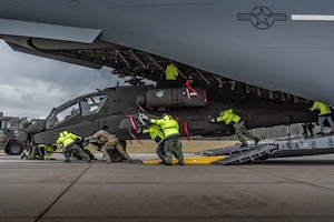 Airmen push a helicopter out of an aircraft onto tarmac on a cloudy day.