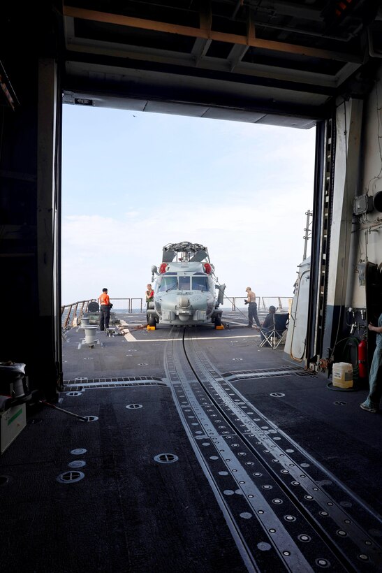 Sailors work on a helicopter aboard a ship at sea.