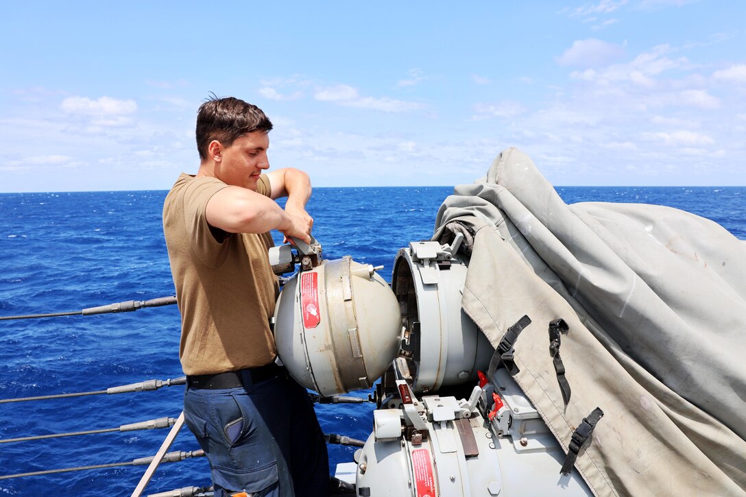A sailor works on a surface vessel torpedo tube aboard a ship at sea.