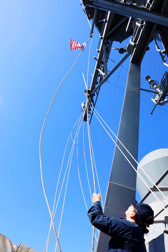 A sailor raises a flag aboard a ship.