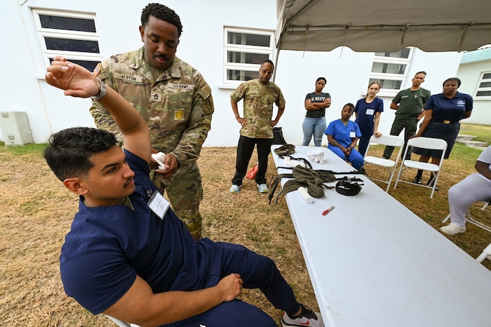 U.S. Army Sgt. 1st Class Luther Alston, 95th Civil Affairs Brigade Medical Operations NCO, demonstrates a bandaging technique on U.S. Air Force Senior Airman Anibal Espinoza, a 433rd Medical Squadron medical technician, outside Joseph N. France General Hospital ins Basseterre, St. Kitts and Nevis, March 25, 2025.