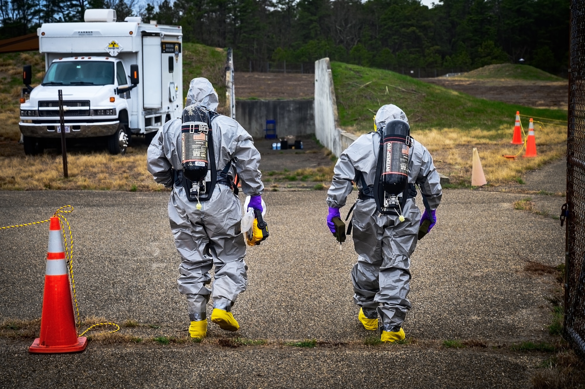 Ryan Petrovic and Eric Troxler, recitation response escorts assigned to the U.S. Army’s 20th Chemical, Biological, Radiological, Nuclear, Explosives (CBRNE) Analytical and Remediation Activity (CARA), prepare to enter an ammunition storage bunker while wearing hazardous materials suits at Joint Base McGuire-Dix-Lakehurst, N.J., April 14, 2025. The CARA recitation response team was tasked to remove an unexploded MK II 75mm projectile with potential chemical components that was discovered at JB MDL. (U.S. Air Force photo by Senior Airman Matt Porter)