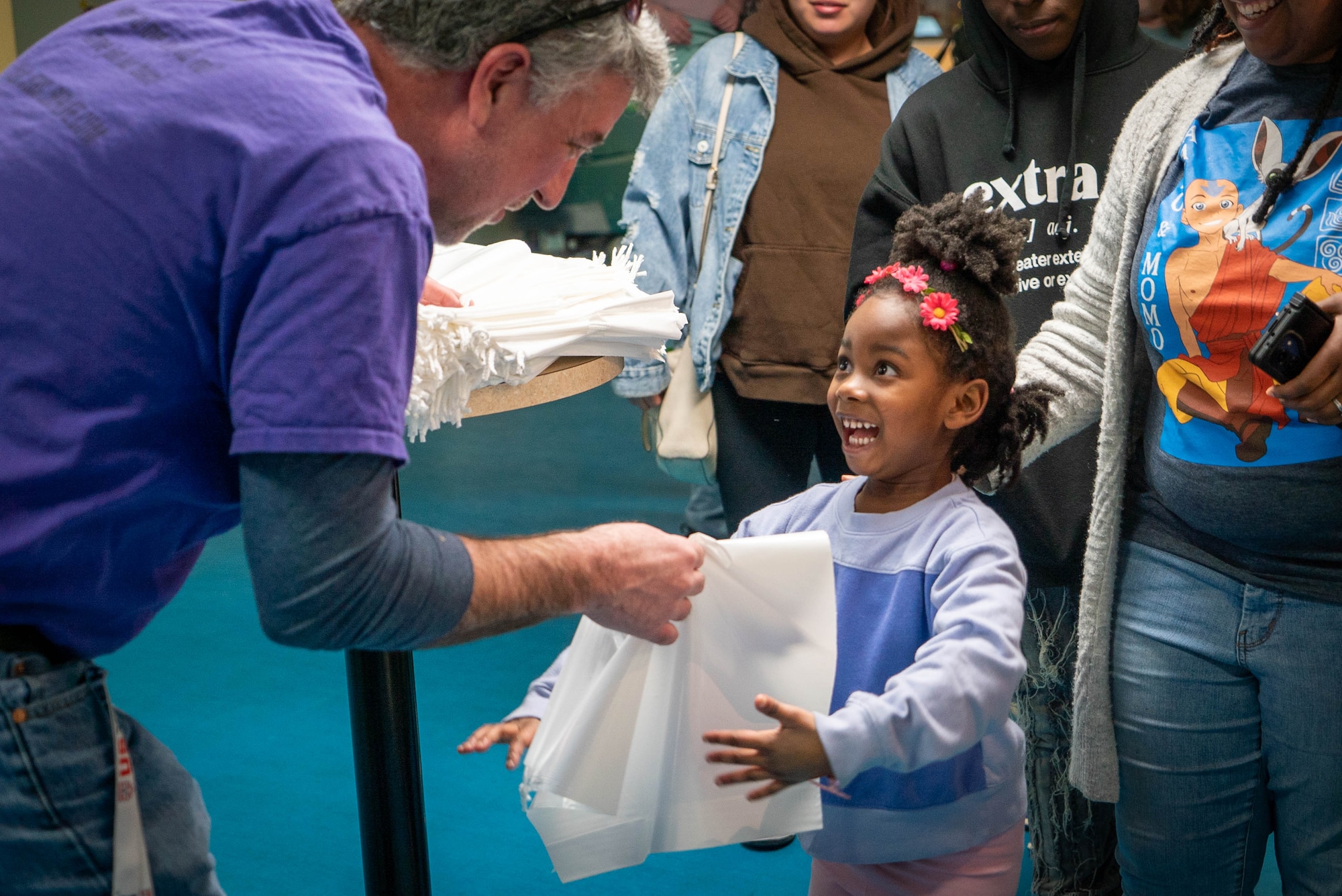 A young girl smiles ecstatically while receiving a plastic bag from an older man.