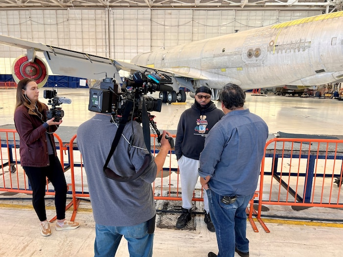 Man being interviewed on camera in front of airplane