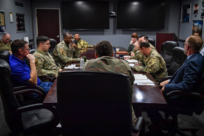 Air Force military members and civilians discuss information at a conference table.