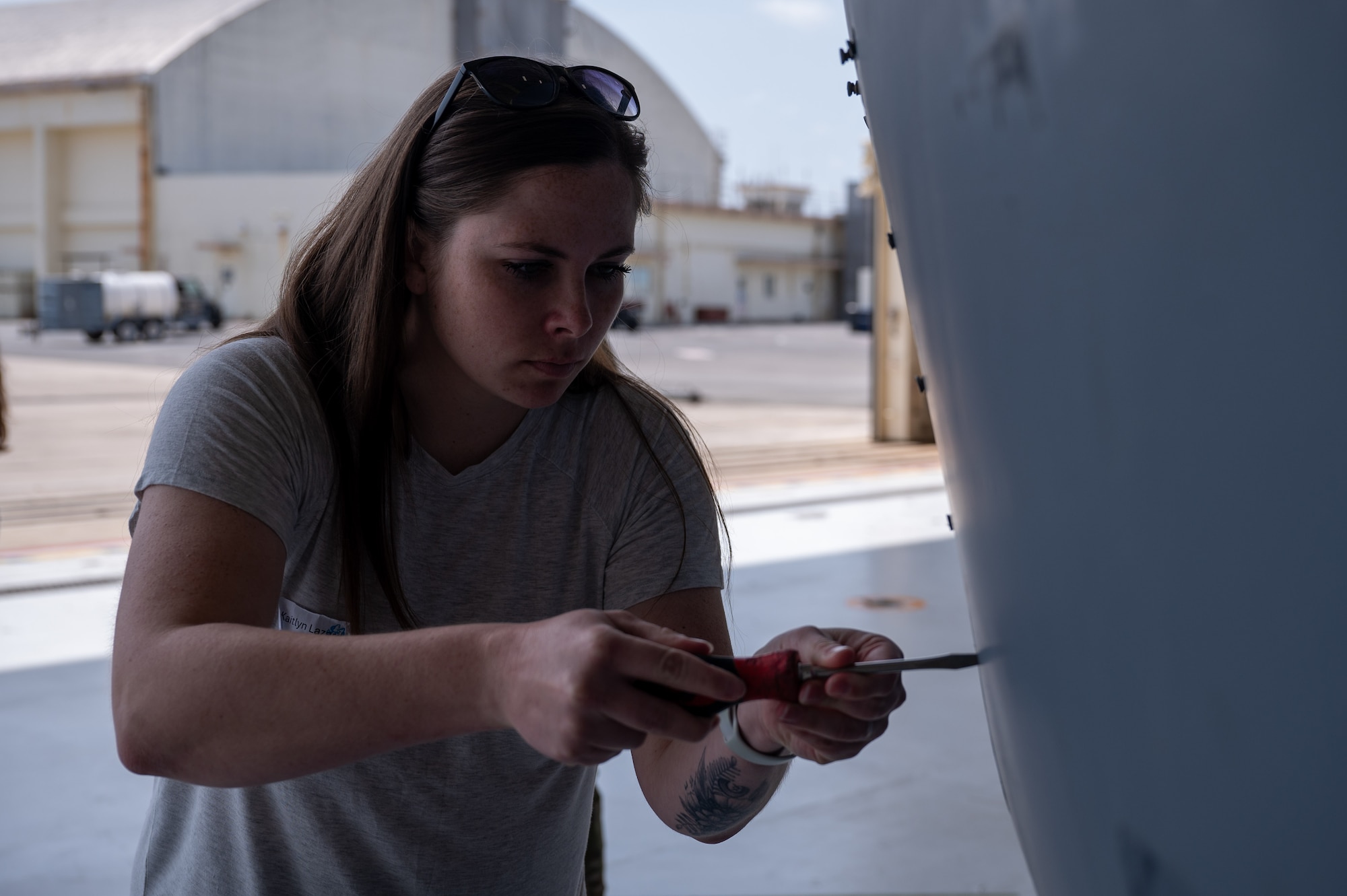 A woman uses a screwdriver to fasten a screw on a piece of an MC-130J in a hangar.