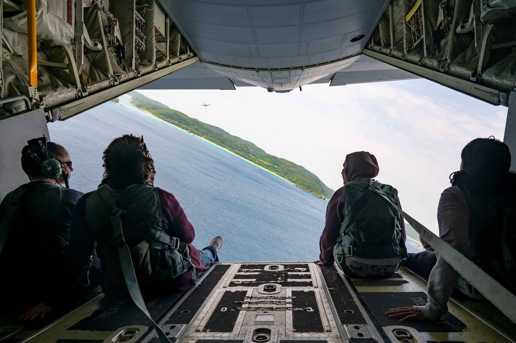 Four people sit on the ramp of an MC-130 and look out of the cargo bay during flight.