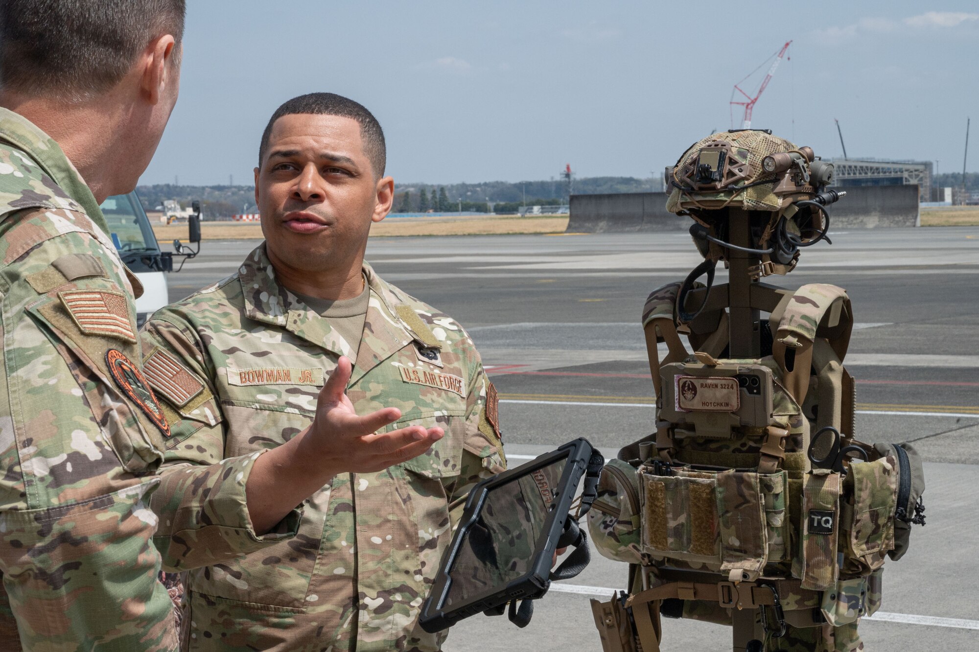 A service member speaks with another service member in front of a helmet and military vest display